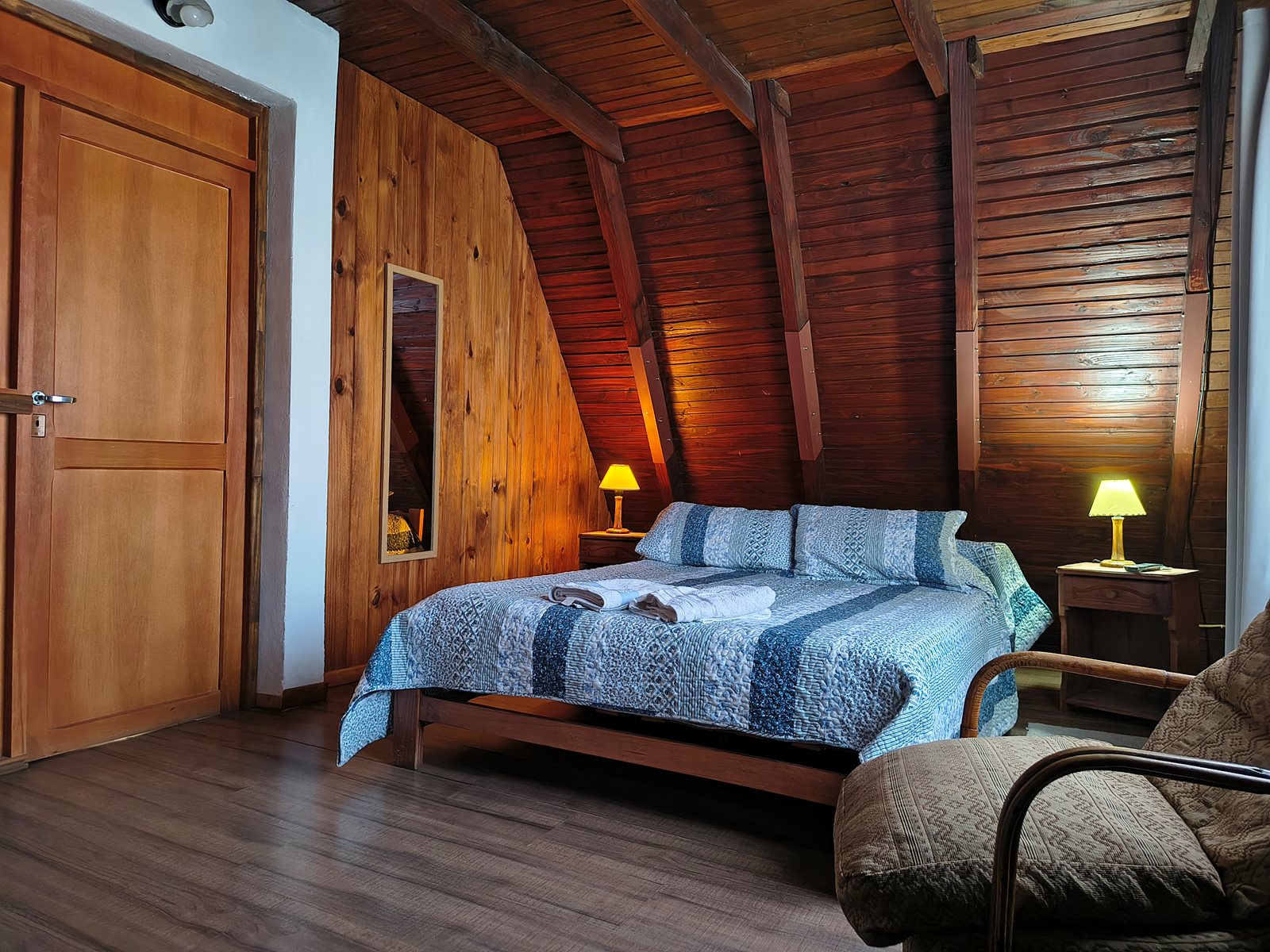 Dormitorio de FREECIS con cama doble, mesas de luz y sillón bajo techo de madera