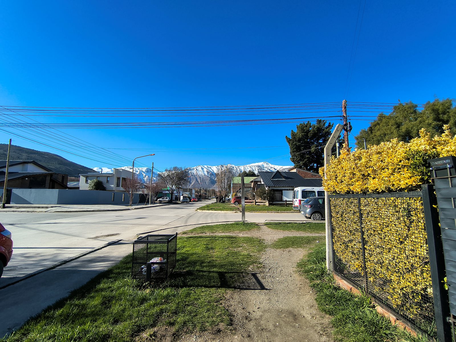 Vista de una calle con casas, vereda y montañas nevadas al fondo